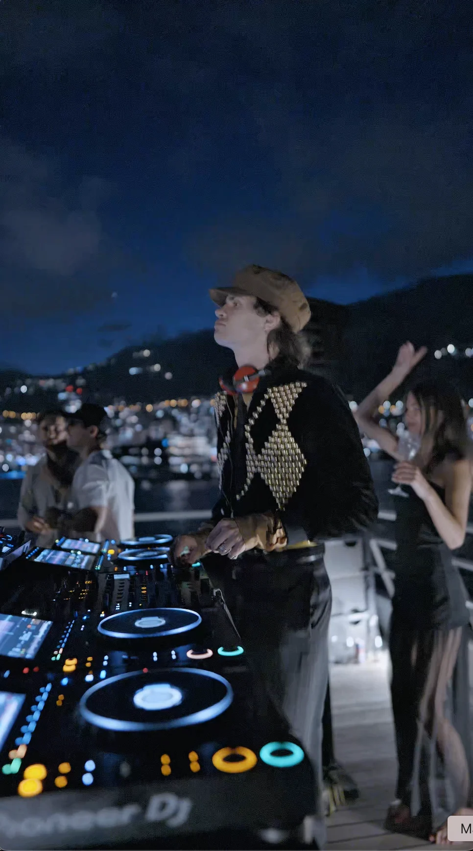 DJ pinchando de noche a bordo, con Mónaco iluminado al fondo