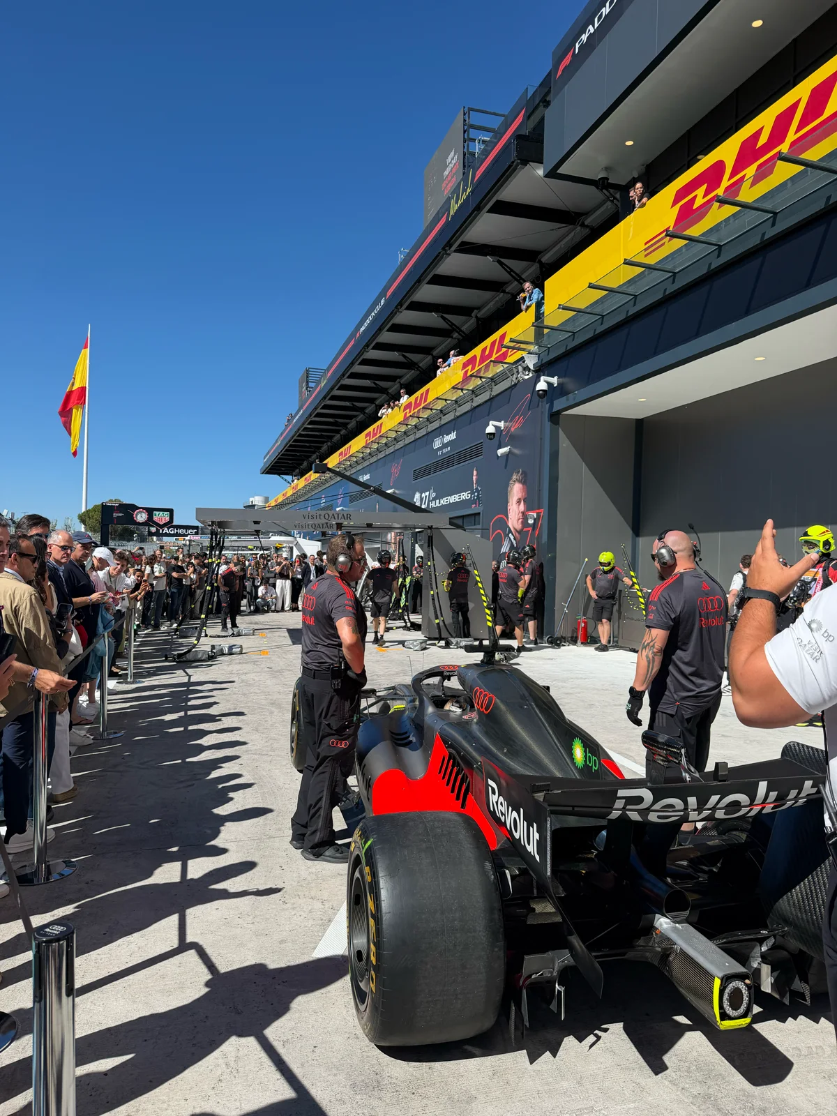 Monoplaza en el pit lane, frente al box, con mecánicos e invitados alrededor